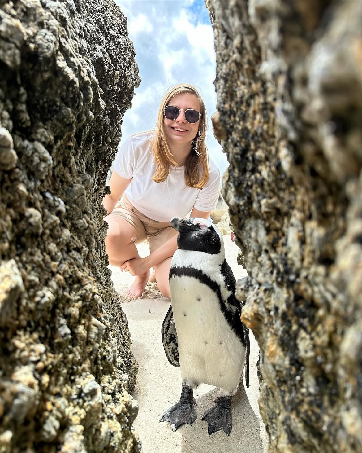 Anastasia crouching next to a penguin between rocks in South Africa